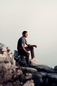 Man sitting on rocks overlooking a calm sea.