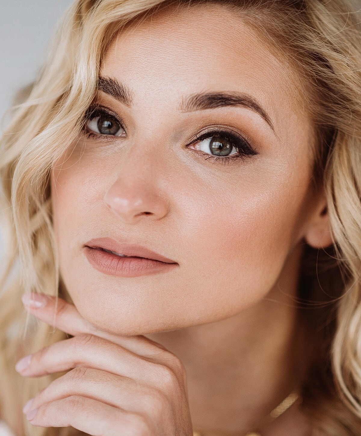 Woman smiling with hand on chin, softly lit.