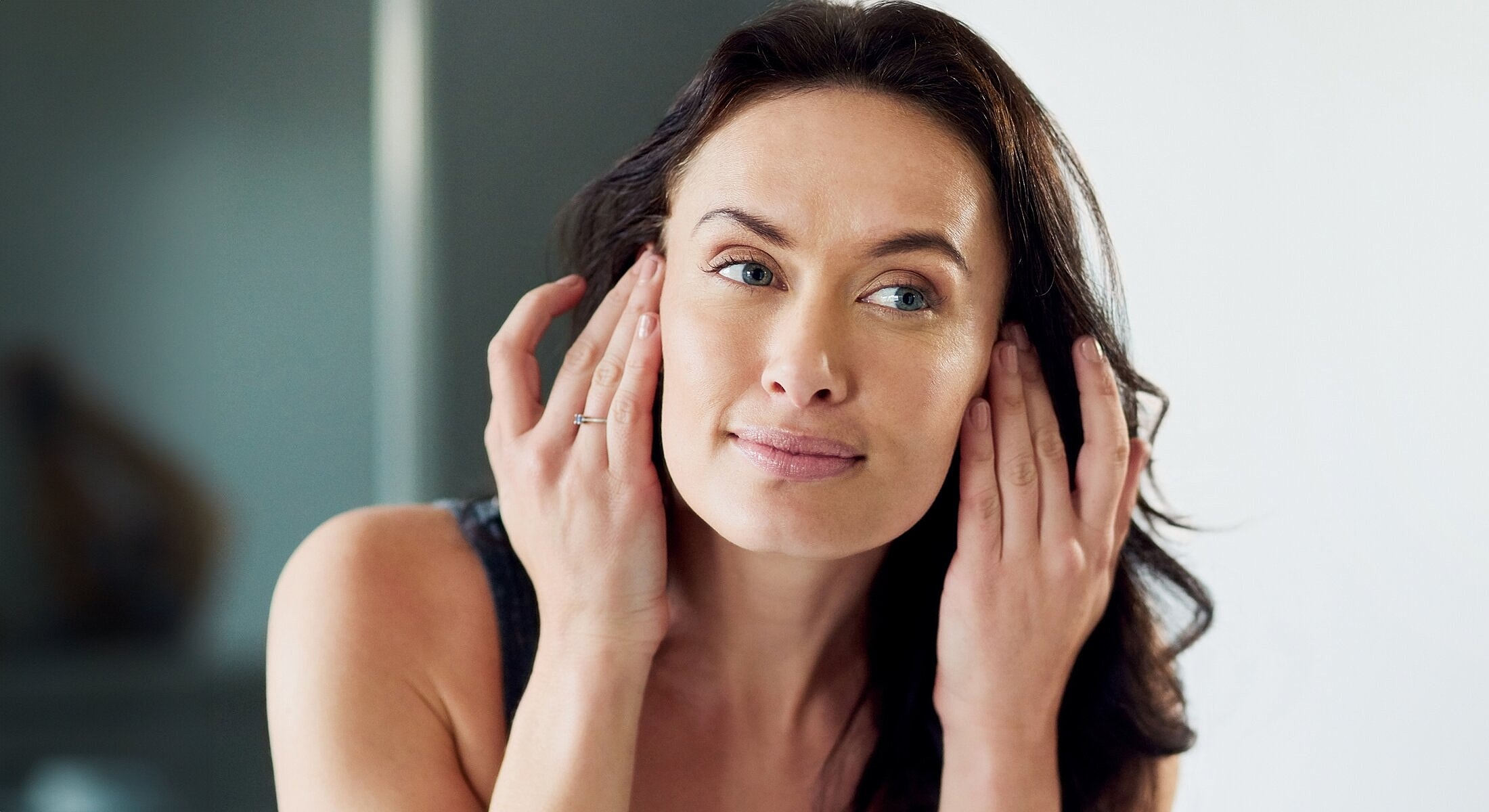 Woman applying skincare in front of mirror.