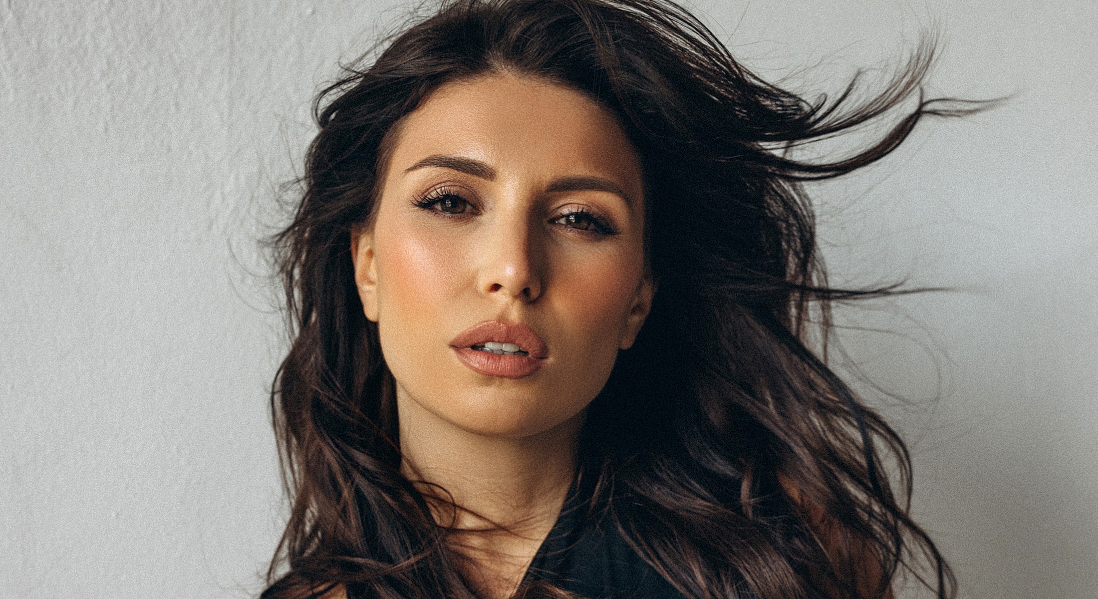 Woman with flowing hair, natural makeup, serious expression.